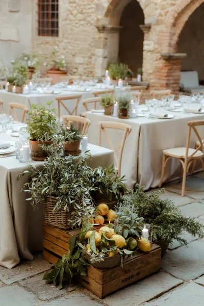 Reception tablescape with outdoor wedding tablescape styling, beige linens, candles, greenery, potted herbs and lemons in a stone courtyard with archways