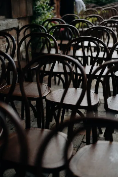 Ceremony seating with wedding ceremony chairs in neat rows, wood chairs with greenery accents against a stone wall on a brick floor
