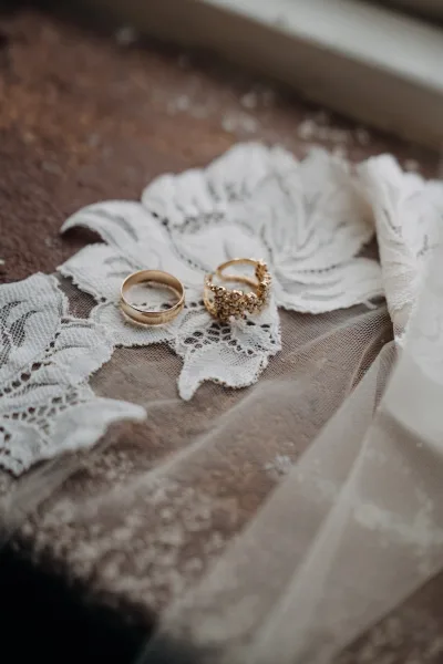 Wedding rings with a gold wedding band and floral cluster ring resting on lace and tulle atop a rustic wooden surface flat lay