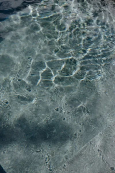 Water texture with sunlight on water, close-up of shallow ripples creating shimmering reflections and soft blue abstract patterns