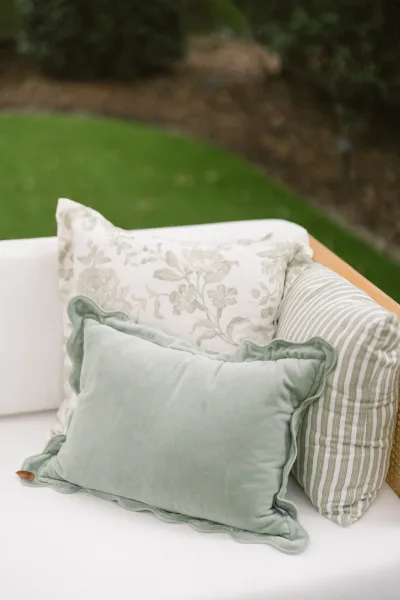 Lounge seating decor with a white upholstered sofa and mixed throw pillows arranged on a grass lawn beside shrubs and mulch ground