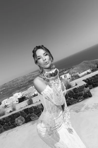 Bridal portrait of a bride blowing a kiss, showcasing an off-the-shoulder neckline against a coastal hillside with ocean view.