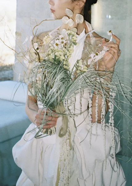 Bridal portrait of a bride holding bouquet with wildflowers and long ribbons, in a strapless dress and veil on a sofa by window light