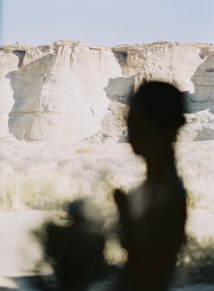 Bridal portrait of a bride holding bouquet in a strapless gown, backlit against white rock cliffs and blue desert sky