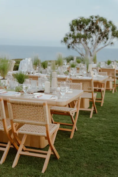 Reception tablescape for outdoor reception decor with greenery centerpieces, set on a grass lawn overlooking the ocean.