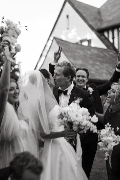 Wedding kiss as newlyweds share a recessional kiss moment outside a church, bride in veil holding bouquet while guests cheer nearby