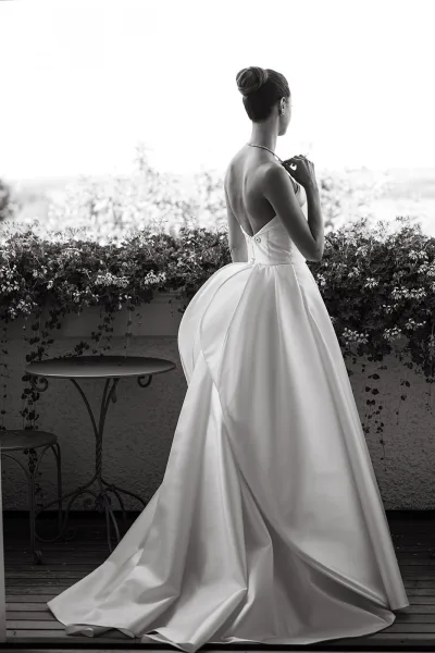 Bridal portrait in black and white of a bride from behind in a strapless satin gown with button back and long train on a vine-lined terrace