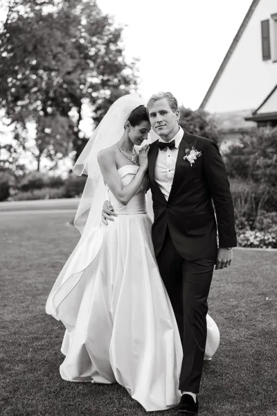 Couple portrait in a black and white wedding portrait style, bride leaning on groom’s arm in veil and tuxedo on a garden lawn