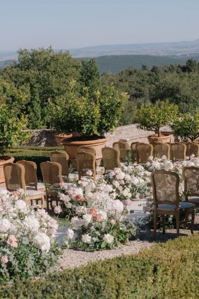 Ceremony setup with garden ceremony seating, featuring cane-back chairs along a gravel aisle, framed by garden trees and a distant mountain view.
