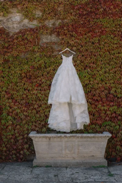 Wedding dress, a lace wedding dress with a scalloped hem, shown against an ivy-covered wall and stone planter.
