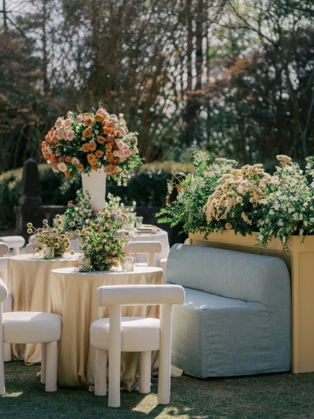 Cocktail hour setup during a garden cocktail hour with pastel floral centerpieces on a grass lawn bordered by hedges and garden trees.